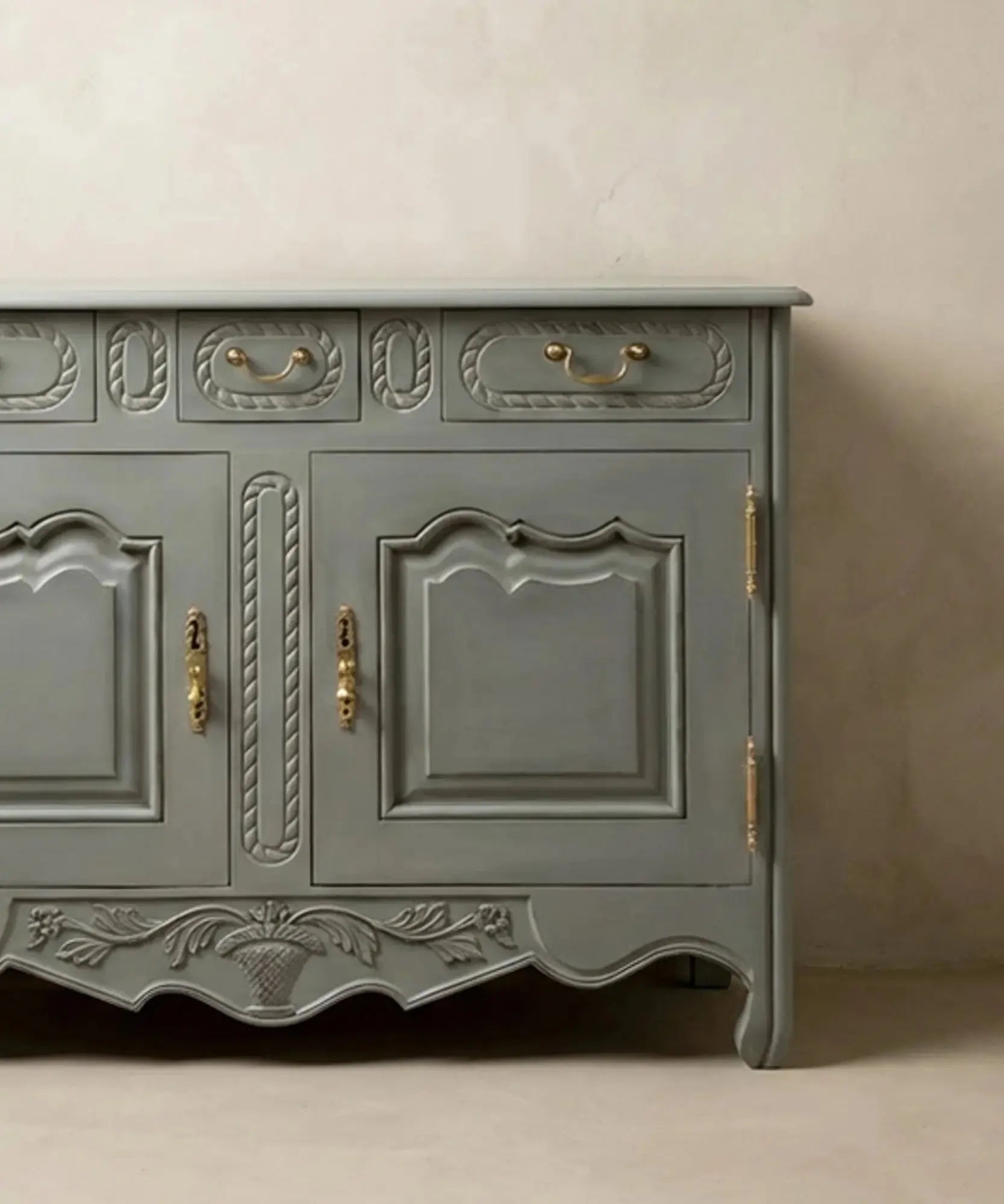 Primer plano de la talla artesanal de cesta floral en el faldón inferior del mueble.
