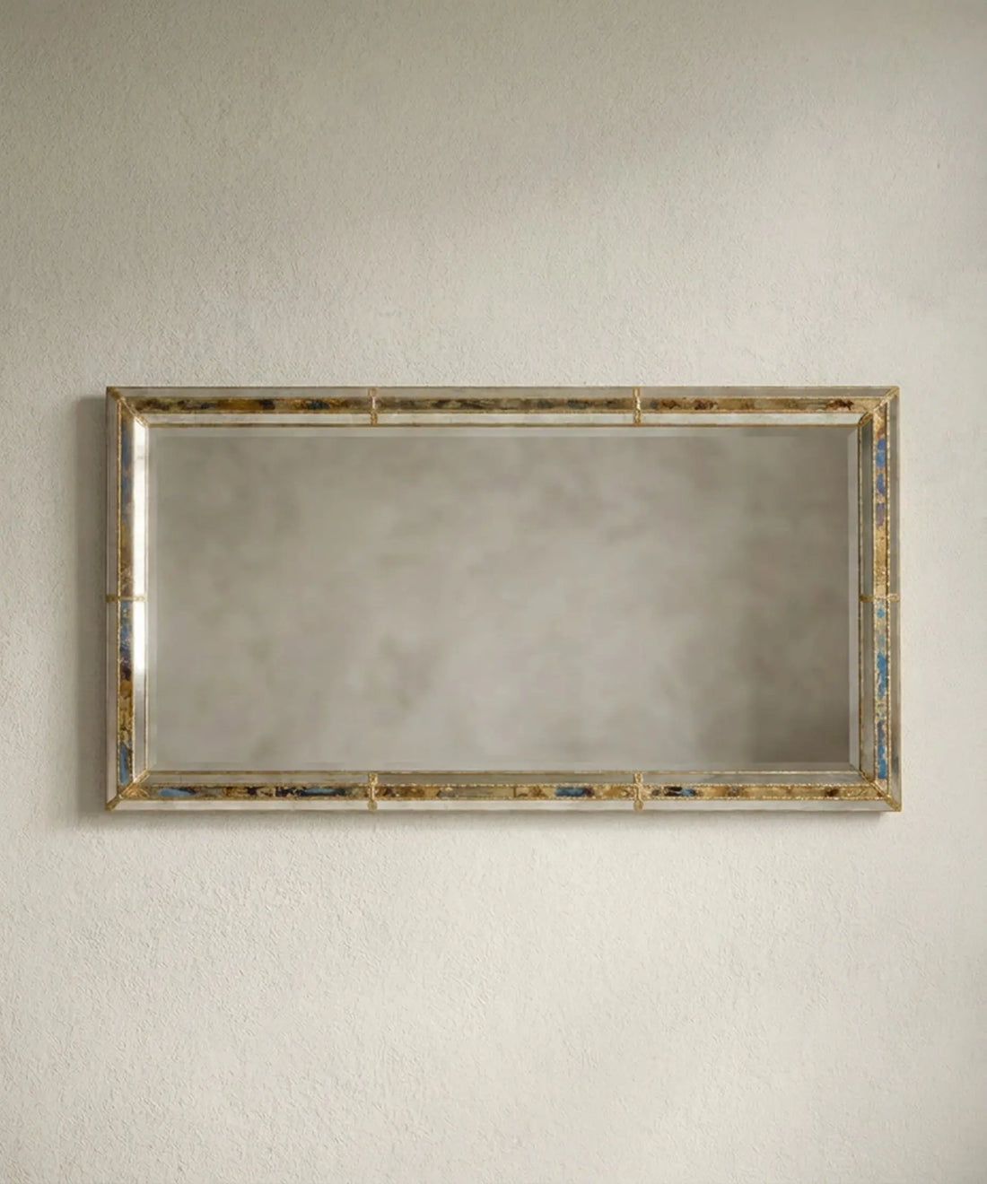Espejo gigante rectangular apoyado en la pared en formato vertical con esquinas de latón dorado.