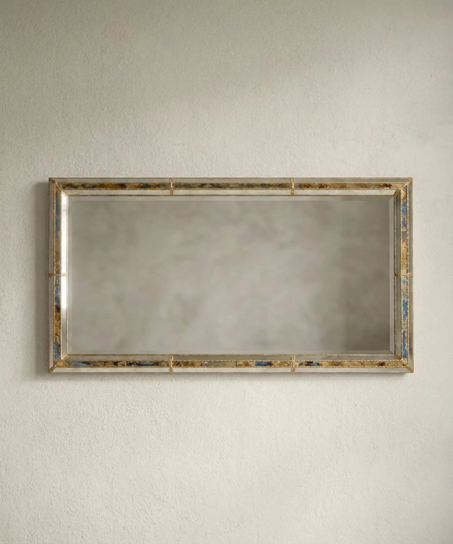 Espejo gigante rectangular apoyado en la pared en formato vertical con esquinas de latón dorado.