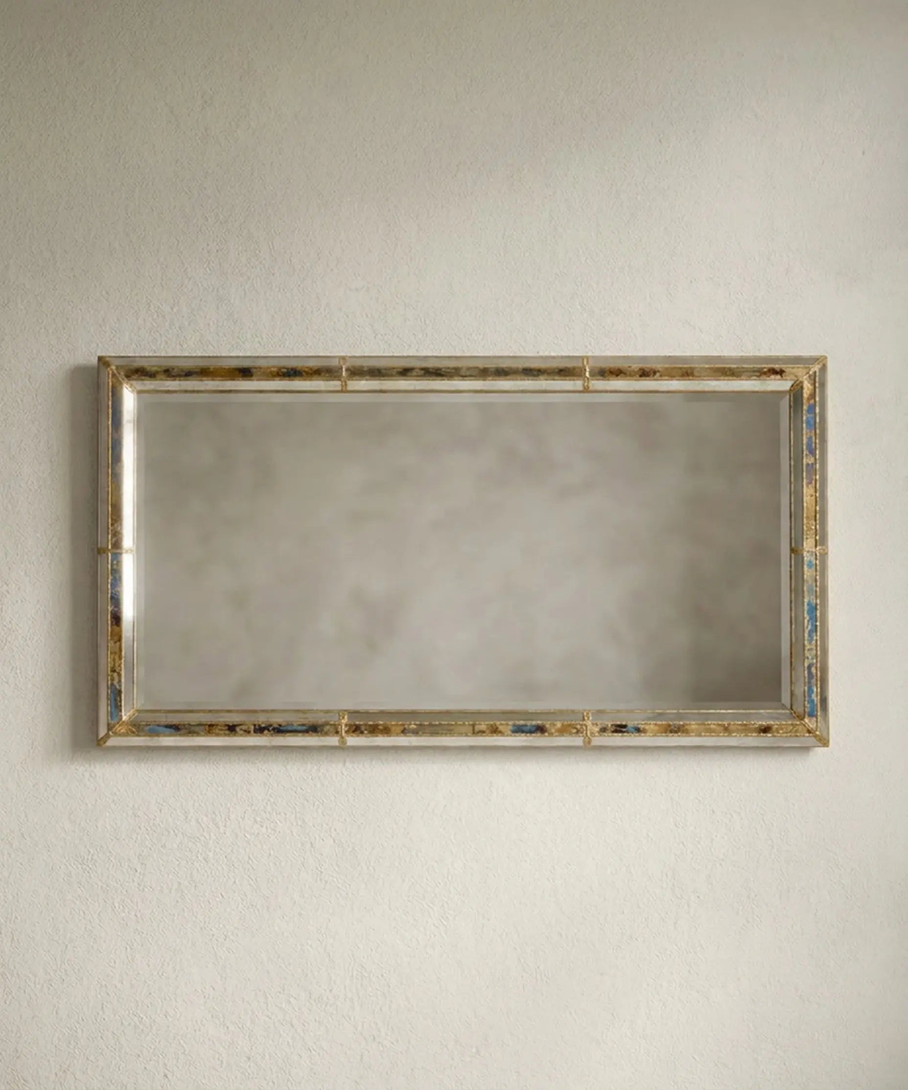 Espejo gigante rectangular apoyado en la pared en formato vertical con esquinas de latón dorado.