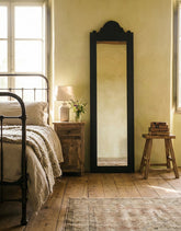 Espejo de cuerpo entero clásico apoyado en pared beige entre dos sillones de cuero marrón y libros en el suelo