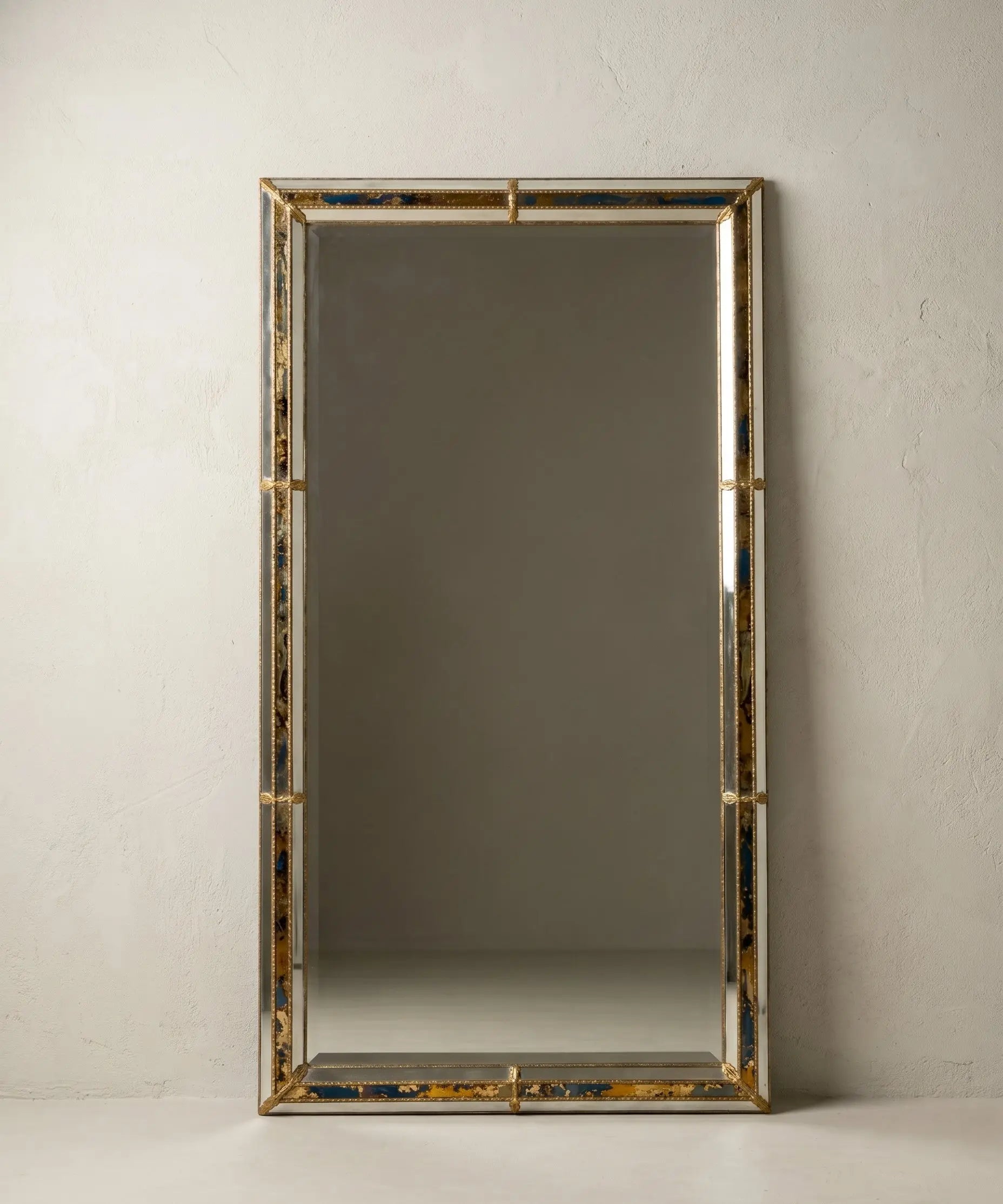 Espejo gigante rectangular apoyado en la pared en formato vertical con esquinas de latón dorado.