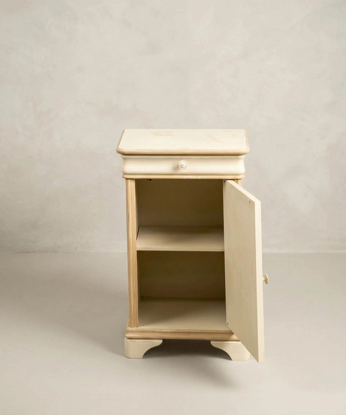 Interior pintado de mesita de noche antigua con cajón abierto y puerta abatible con balda.