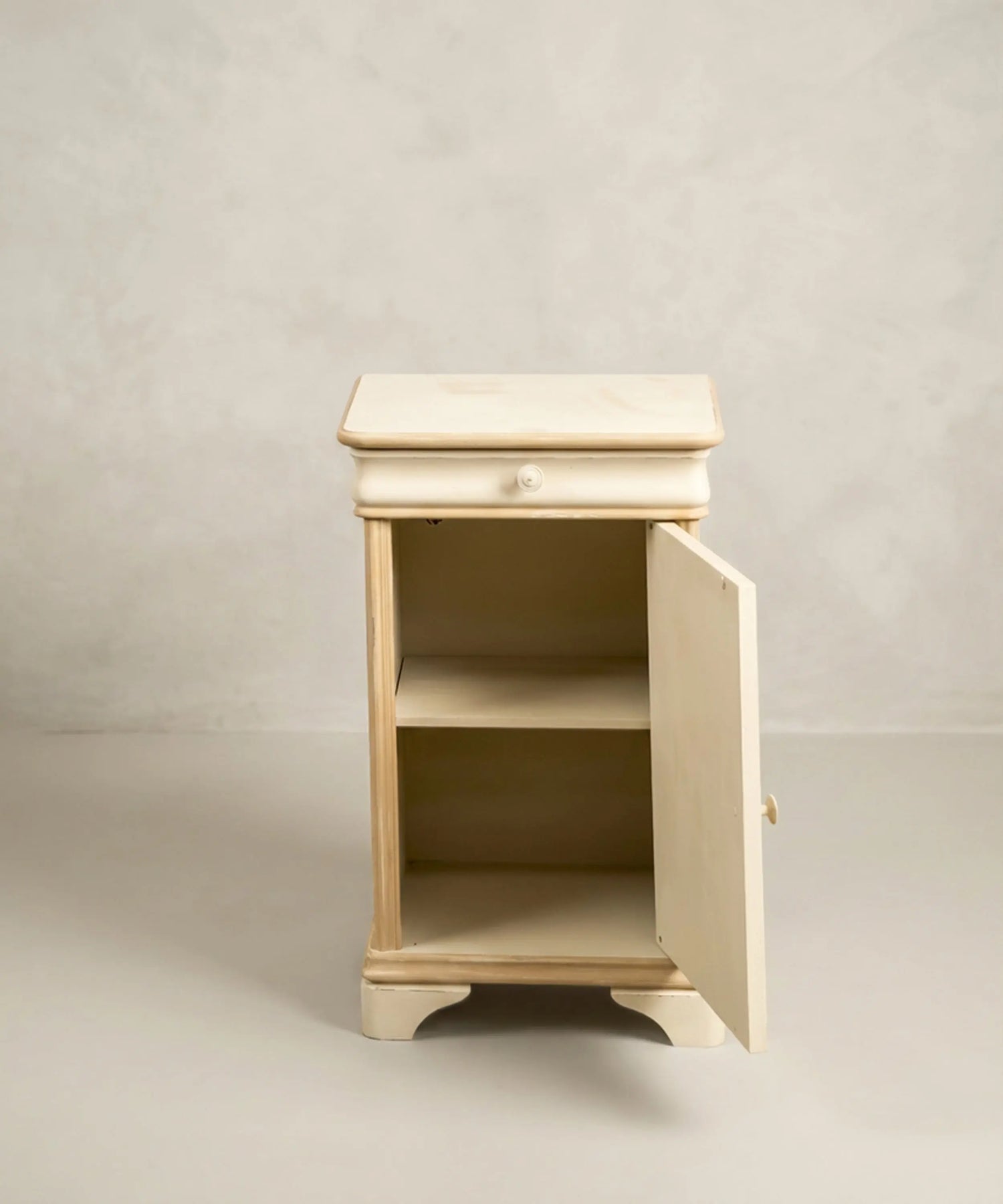 Interior pintado de mesita de noche antigua con cajón abierto y puerta abatible con balda.