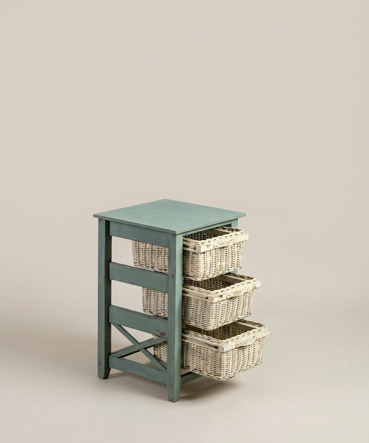 Vista general de la cajonera auxiliar de madera azul con tres cestas de mimbre blancas sobre fondo neutro