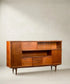 Aparador Mid-Century Modern de teca con puertas y vitrina frontal sobre fondo neutro.