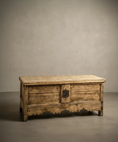 Vista lateral de baúl antiguo de madera clara resaltando la veta natural y estructura robusta.