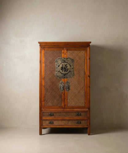 Armario chino de madera cálida y paneles de ratán con herraje central de latón sobre fondo neutro.