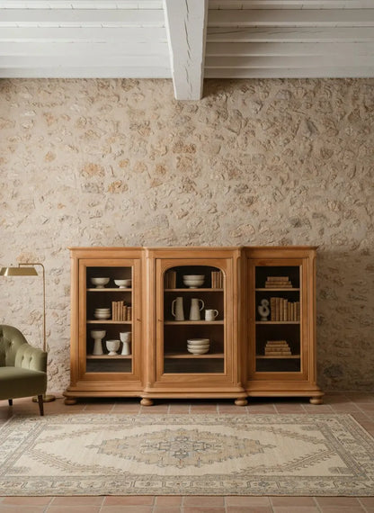 Vitrina de madera maciza decorada con vajilla blanca frente a una pared de piedra rústica.