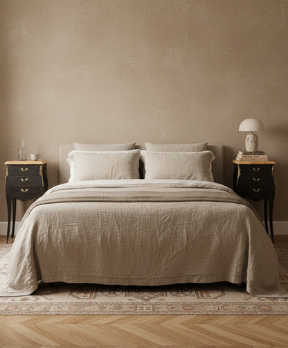 Mesillas de estilo francés flanqueando una cama de lino, mostrando su escala y presencia en un dormitorio clásico moderno.