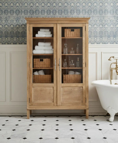 Vitrina de madera clara estilo provenzal con puertas de cristal y herrajes ornamentados decorada en baño de piso clásico.