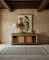 Composición decorativa del aparador bajo con lámpara de mesa y cuadro abstracto en salón de muros de piedra.