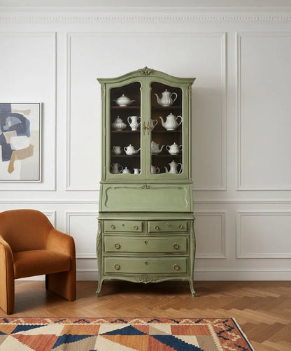 Bureau verde salvia decorando un salón clásico contemporáneo con libros antiguos y decoración sofisticada.