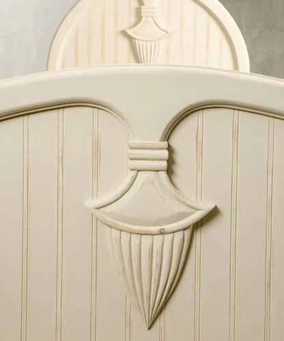 Primer plano del medallón neoclásico tallado a mano en el cabecero de la cama con acabado decapado.