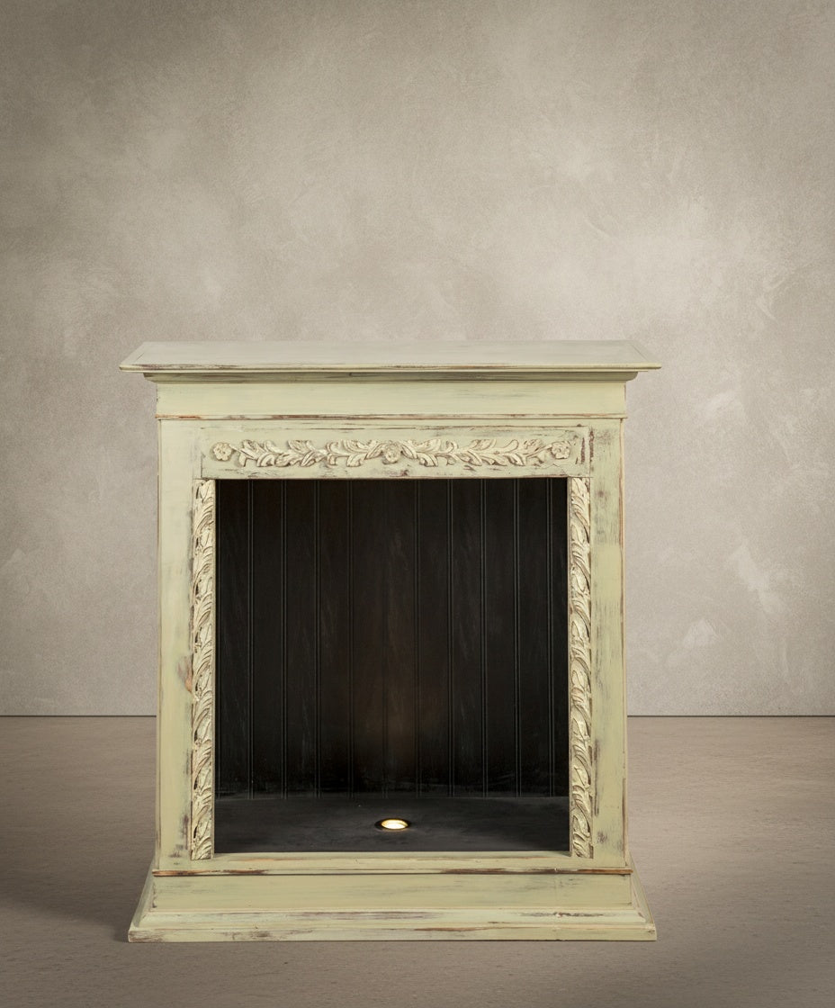  Vista frontal de la chimenea decorativa verde pátina con talla floral sobre fondo neutro.