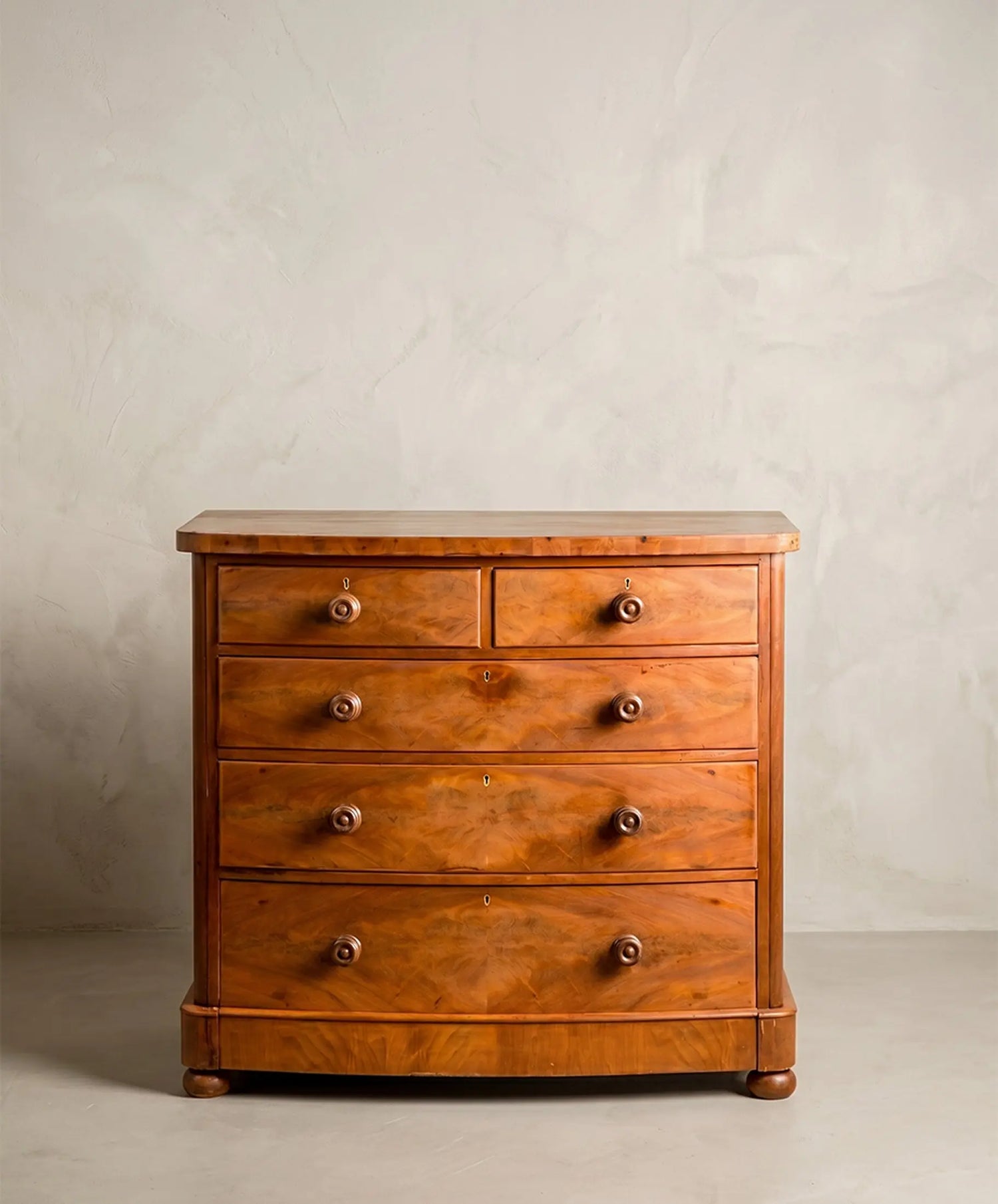 Cómoda inglesa antigua de frente curvo en madera de caoba con cinco cajones y tiradores torneados.