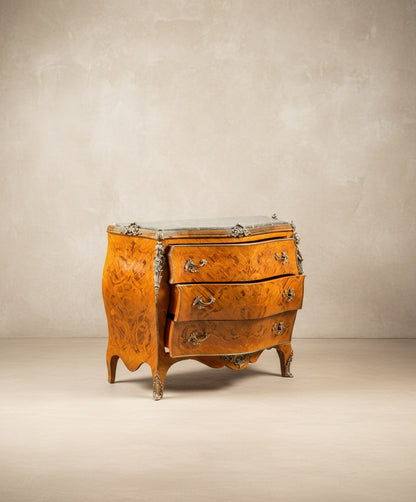 Vista angular de la cómoda resaltando la curvatura lateral y los herrajes de bronce cincelado.