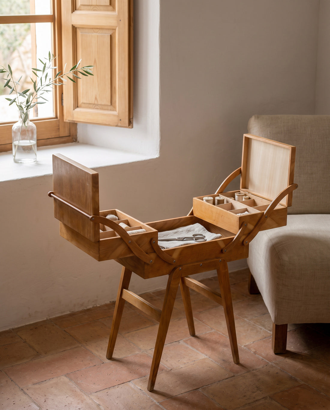 Costurero vintage abierto junto a butaca de lino en salón con suelo de barro — Antique Arte y Decoración