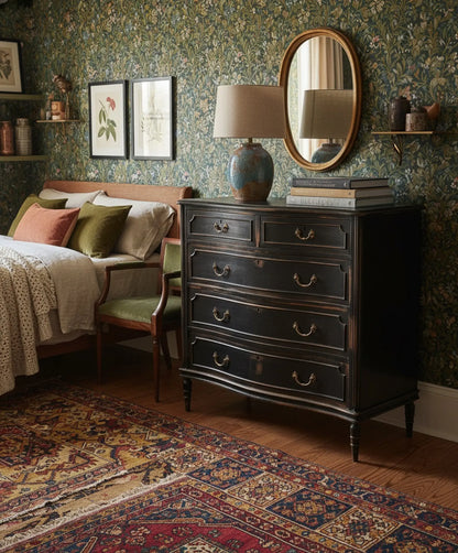 Dormitorio elegante con papel pintado y cómoda clásica restaurada en negro con tiradores de latón.