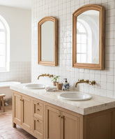 Dos espejos de madera arqueados colocados sobre lavabo doble en baño de estilo mediterráneo