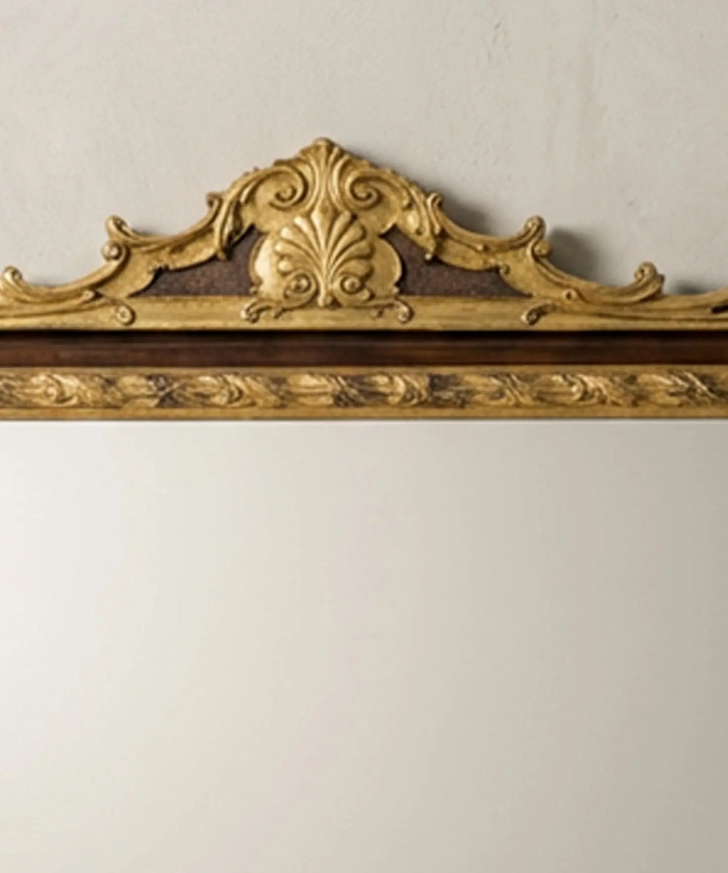 "Detalle de talla en madera dorada con forma de concha y hojas de acanto en la parte superior del espejo."