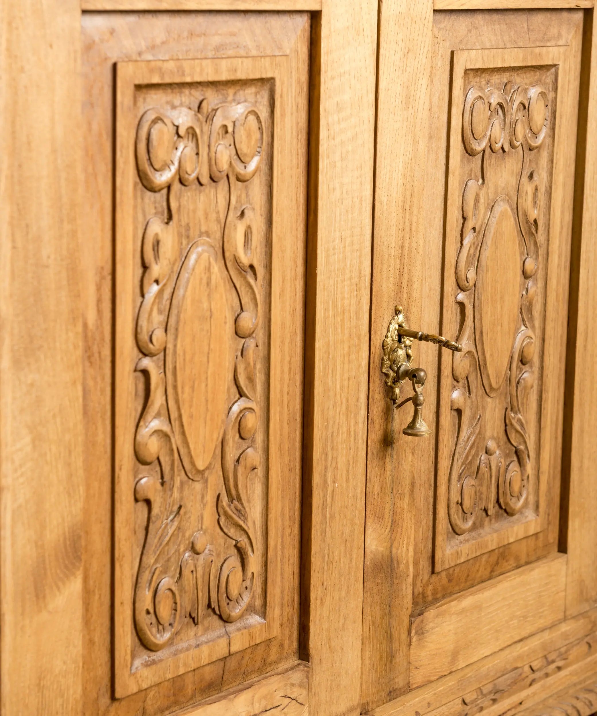 Primer plano de talla de madera en relieve y tirador de latón colgante antiguo sobre madera lavada.