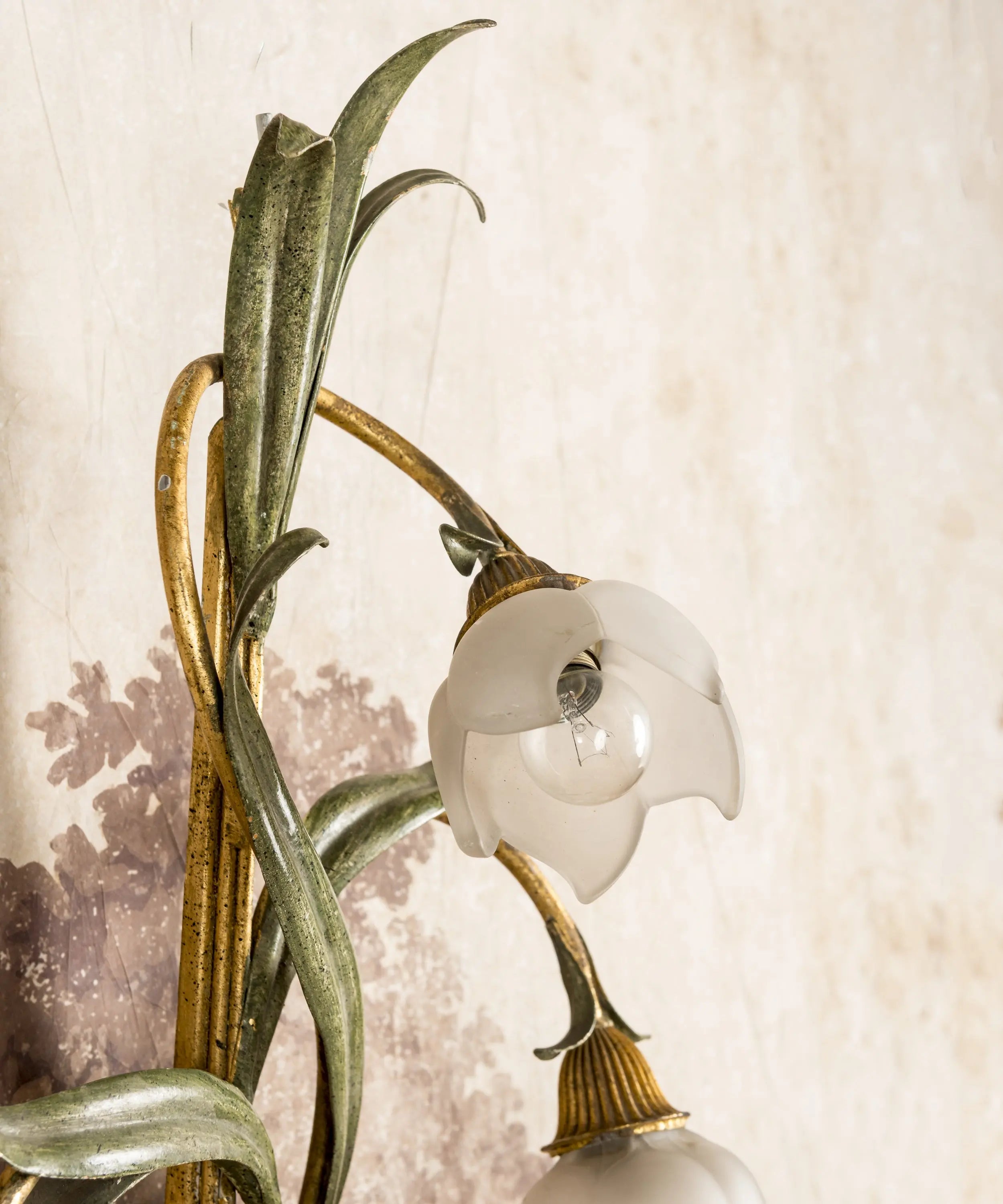 Primer plano de tulipa de cristal esmerilado en forma de flor sobre tallo de forja verde y dorada.