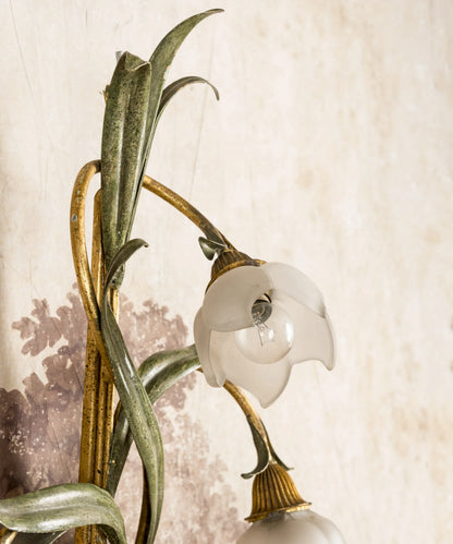 Primer plano de tulipa de cristal esmerilado en forma de flor sobre tallo de forja verde y dorada.