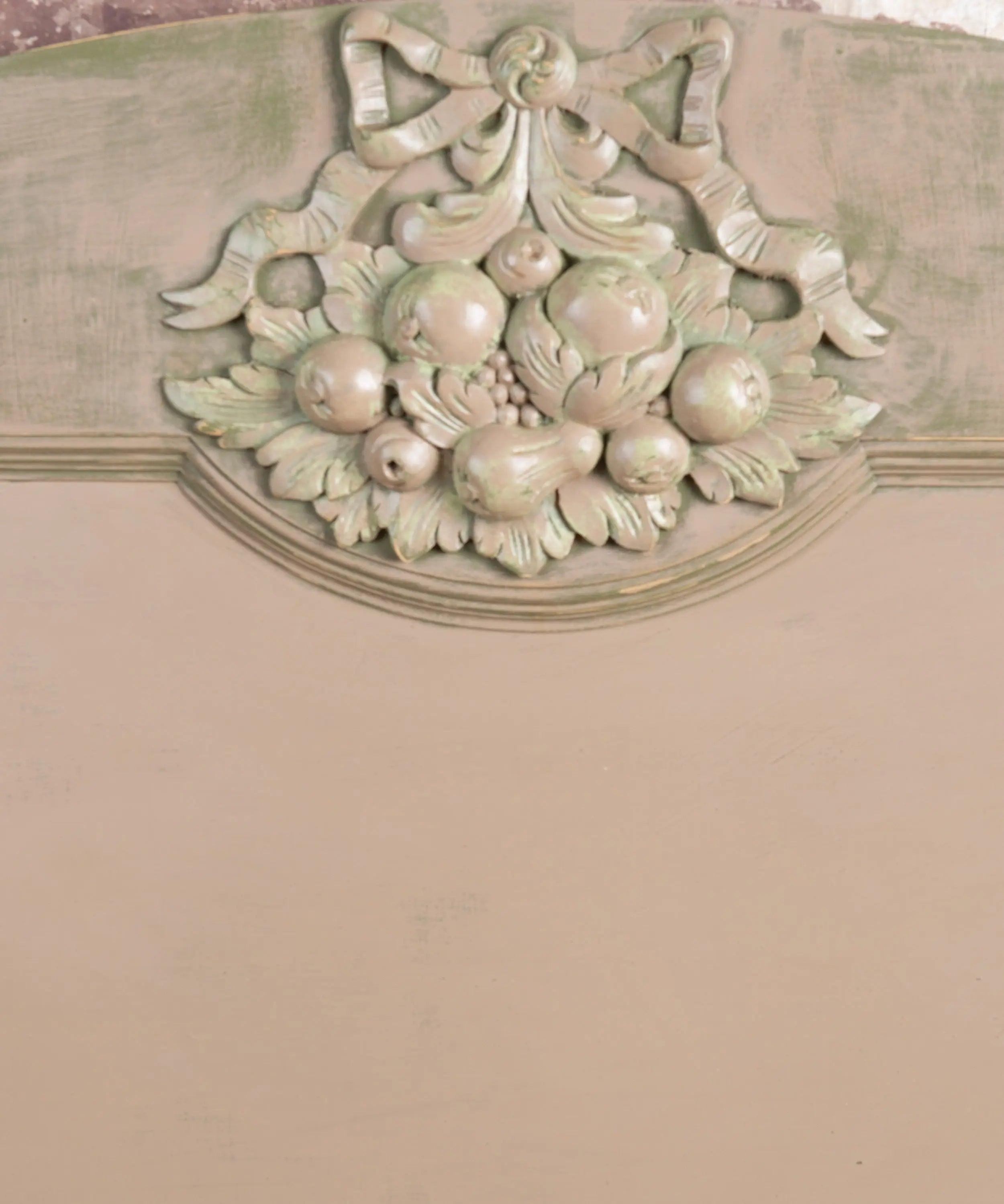 Primer plano de talla clásica de madera con frutas y lazo en cabecero de cama patinado en verde y crema.