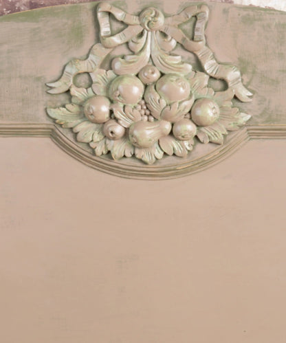 Primer plano de talla clásica de madera con frutas y lazo en cabecero de cama patinado en verde y crema.
