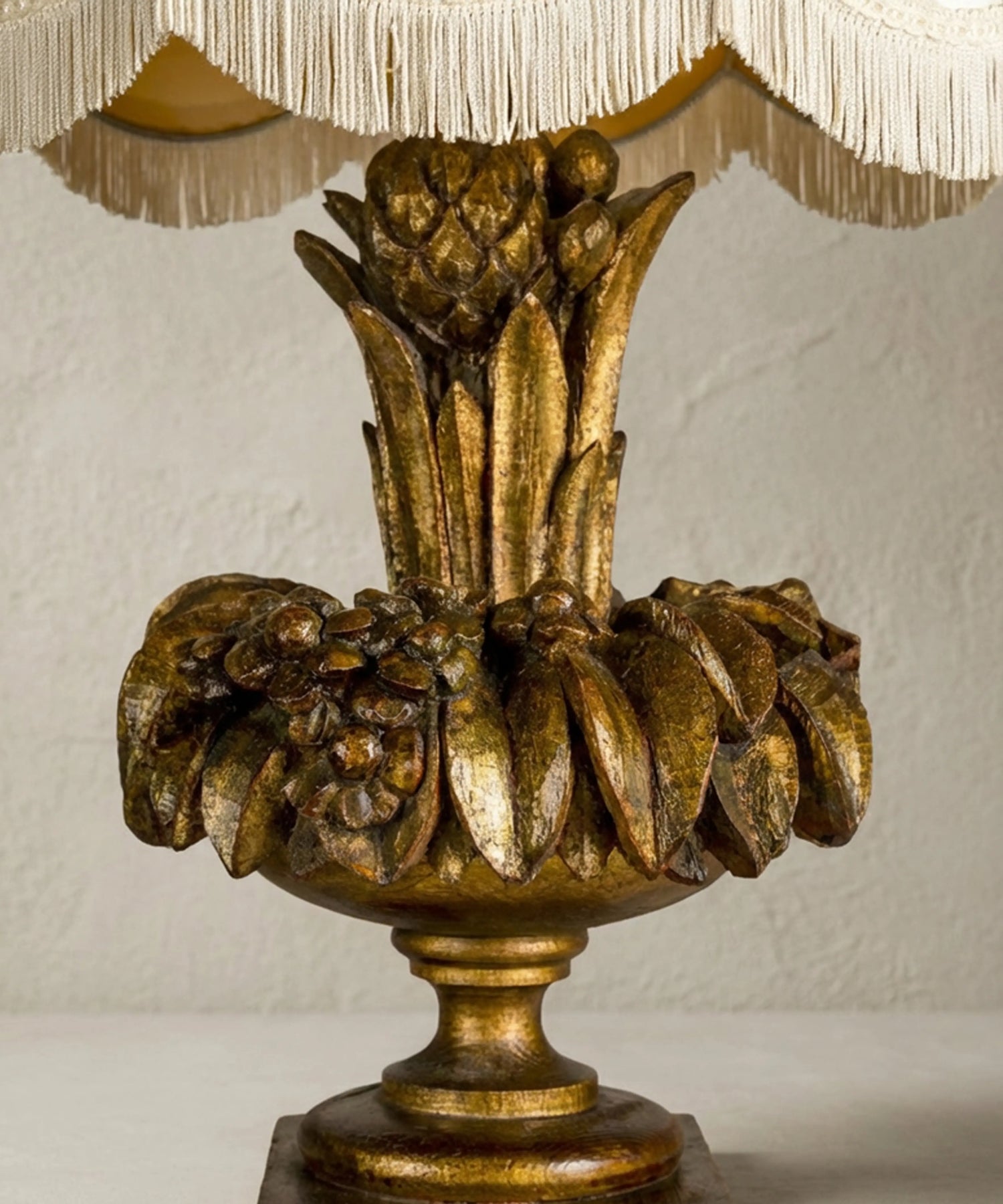 Primer plano de exuberante talla floral y frutal en madera con pan de oro envejecido en lámpara antigua.