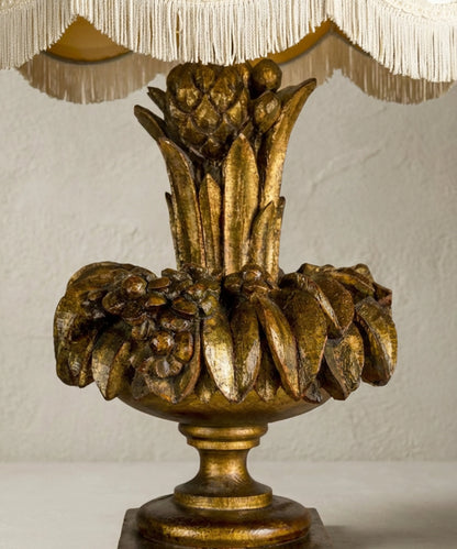 Primer plano de exuberante talla floral y frutal en madera con pan de oro envejecido en lámpara antigua.