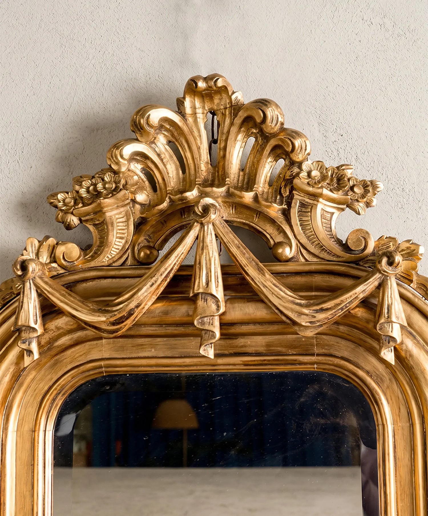 Detalle macro del copete tallado del espejo antiguo mostrando el pan de oro, las volutas de acanto y la cenefa de paños colgantes.