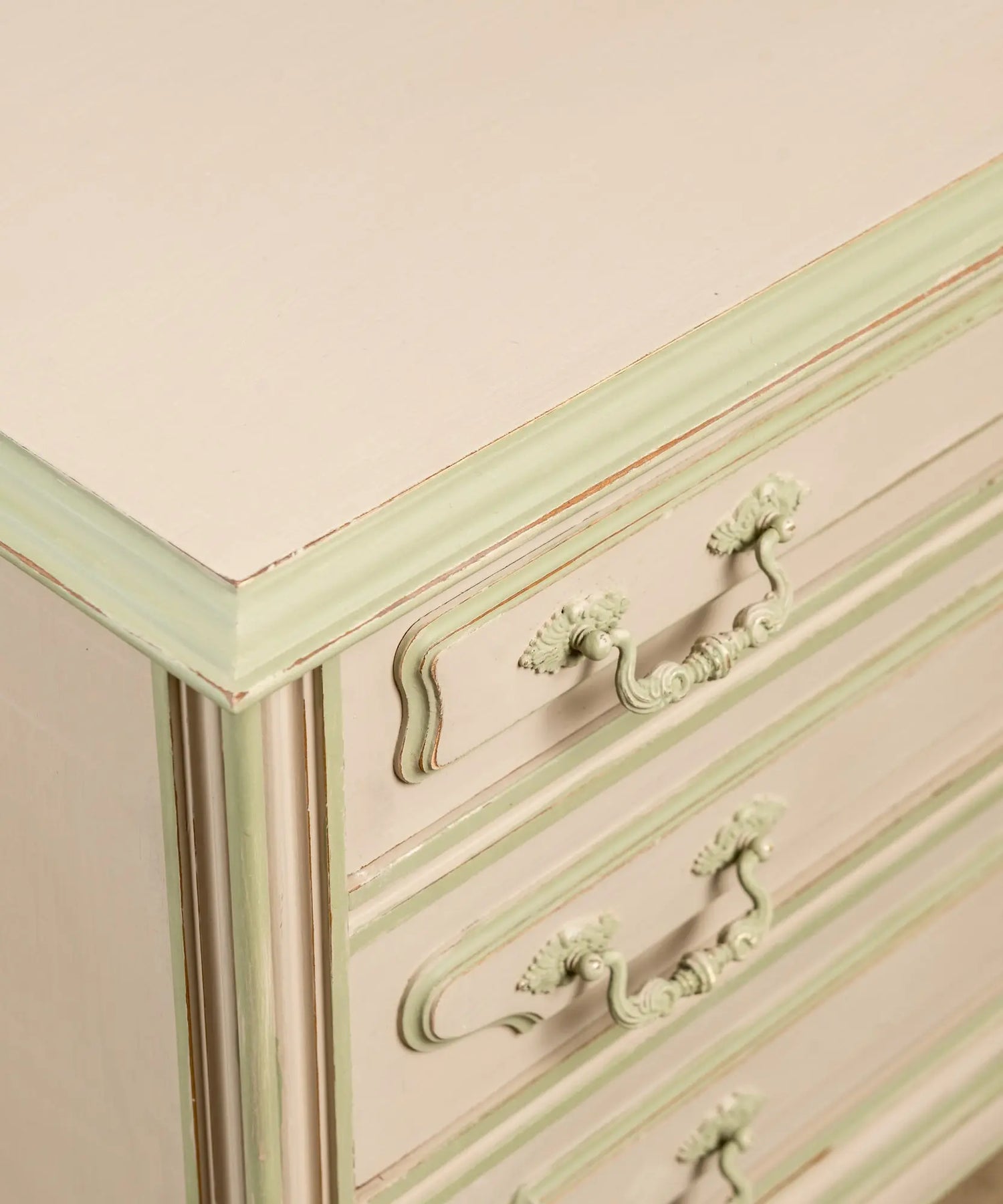 Primer plano de tiradores clásicos y molduras pintadas en verde sobre cajones color beige arena.