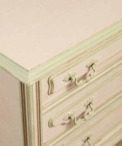 Primer plano de tiradores clásicos y molduras pintadas en verde sobre cajones color beige arena.