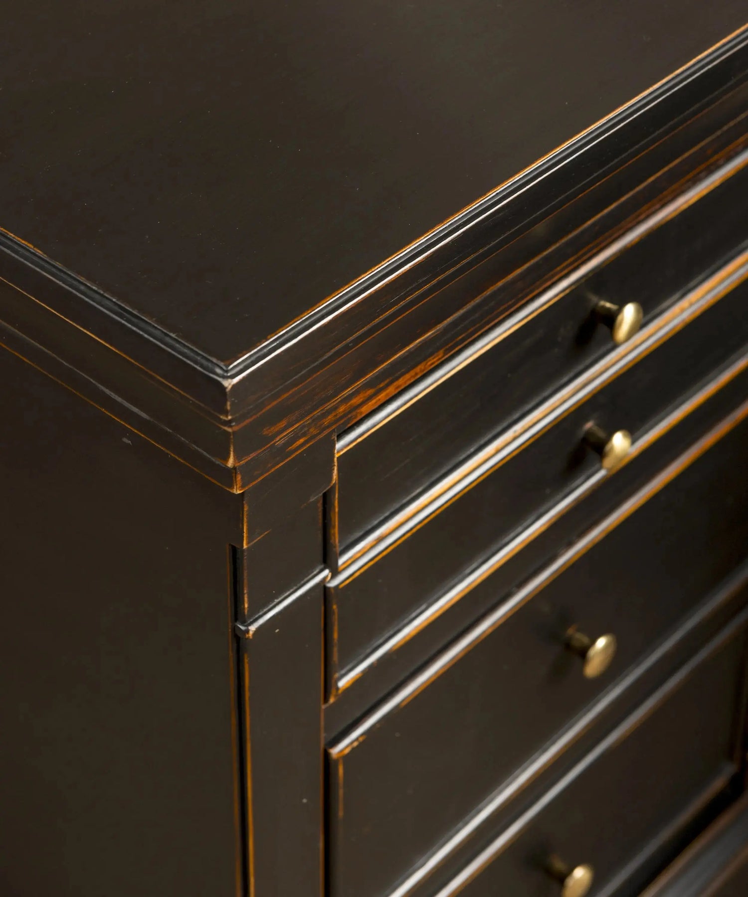 Primer plano del acabado decapé revelando la madera bajo la pintura negra en una mesita antigua.