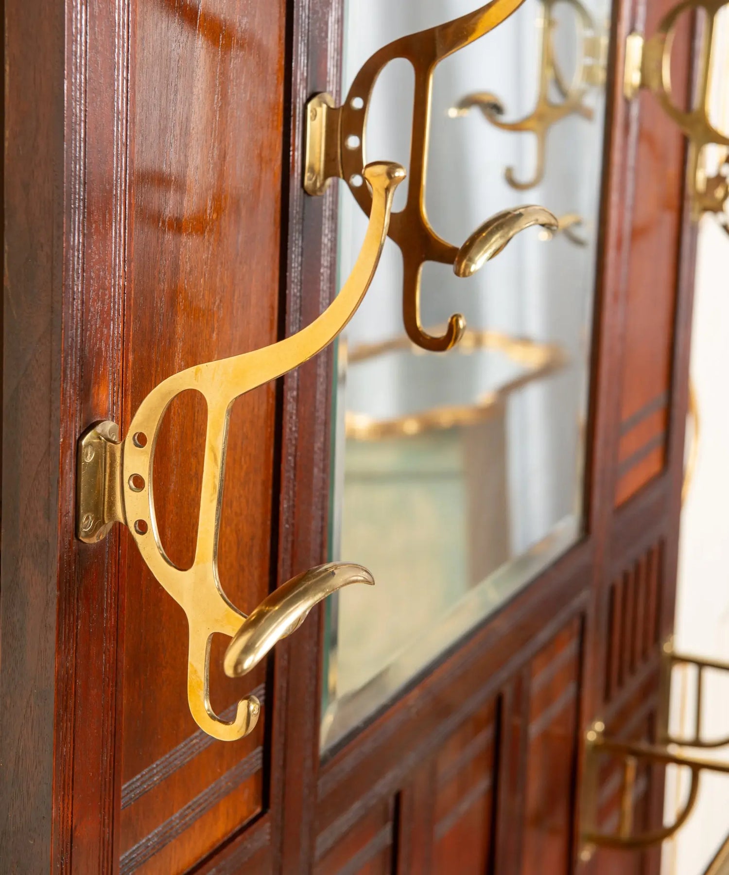 Primer plano de percha curva de bronce macizo pulido sobre madera de caoba antigua.