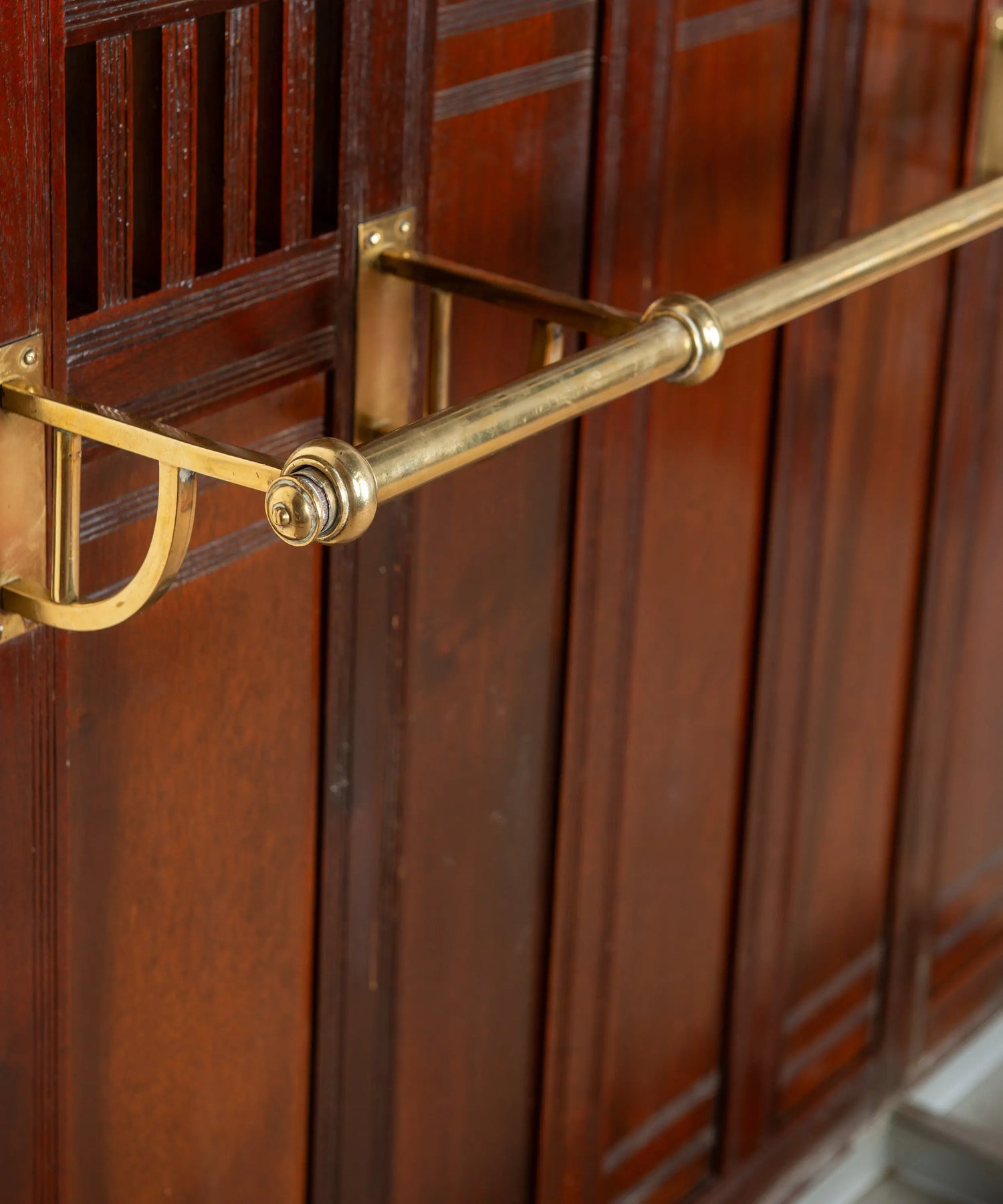Primer plano de percha curva de bronce macizo pulido sobre madera de caoba antigua.