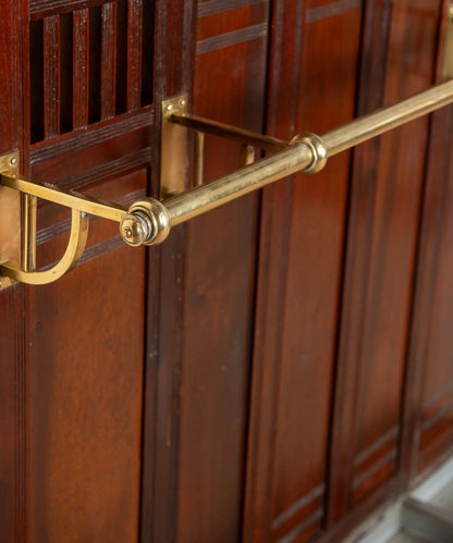 Primer plano de percha curva de bronce macizo pulido sobre madera de caoba antigua.