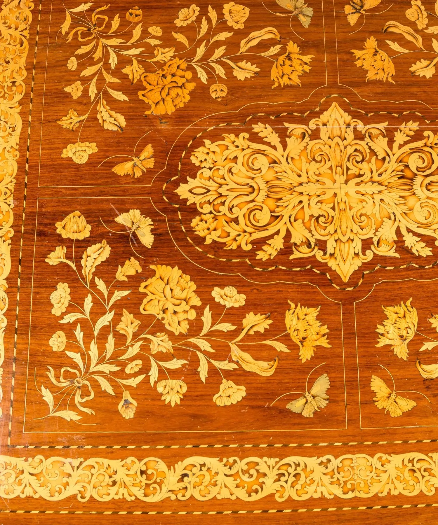 Primer plano de centro de mesa antiguo con incrustaciones artesanales de hojas de acanto y flores en madera clara.