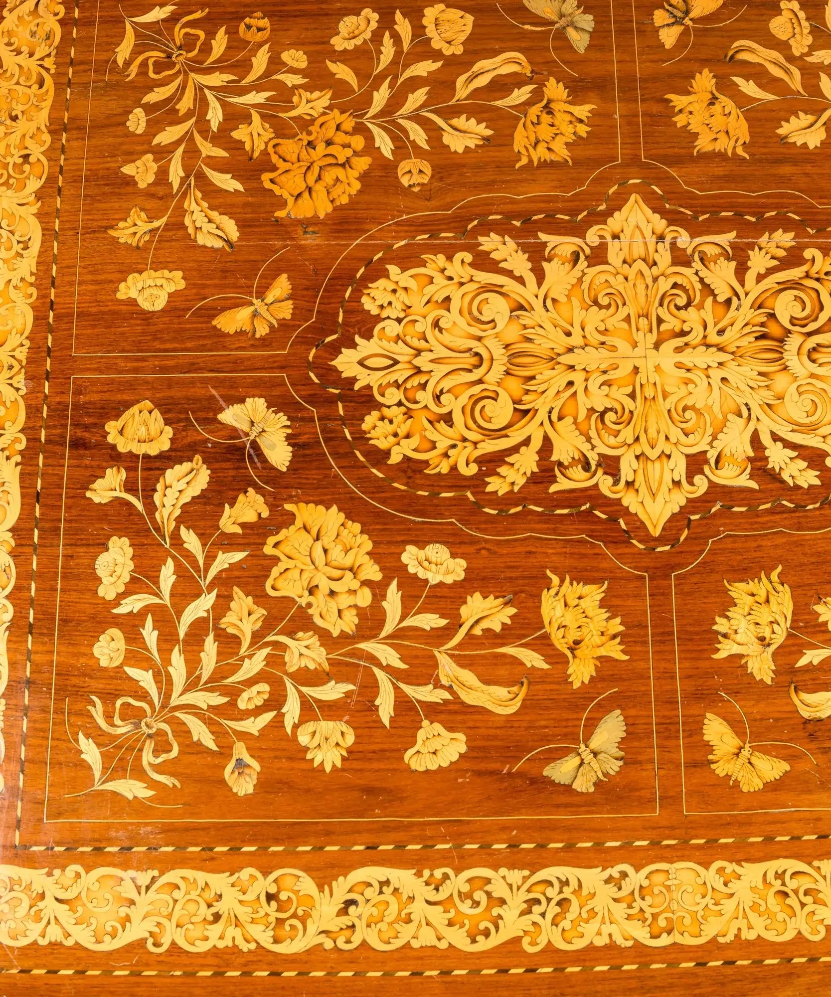 Primer plano de centro de mesa antiguo con incrustaciones artesanales de hojas de acanto y flores en madera clara.