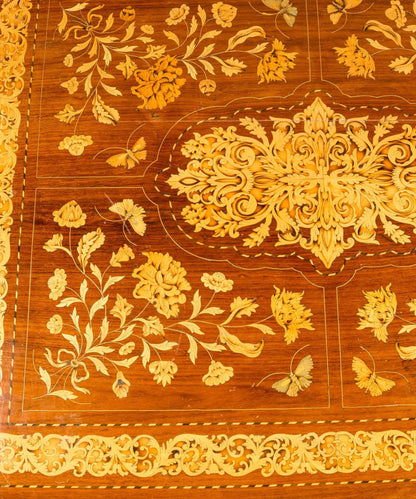 Primer plano de centro de mesa antiguo con incrustaciones artesanales de hojas de acanto y flores en madera clara.