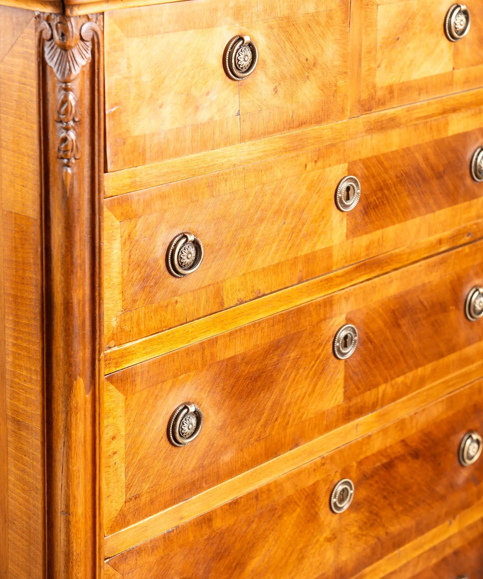 Detalle de chapa de madera dispuesta en espiga (frisage) y tiradores de anilla clásicos en mueble antiguo.