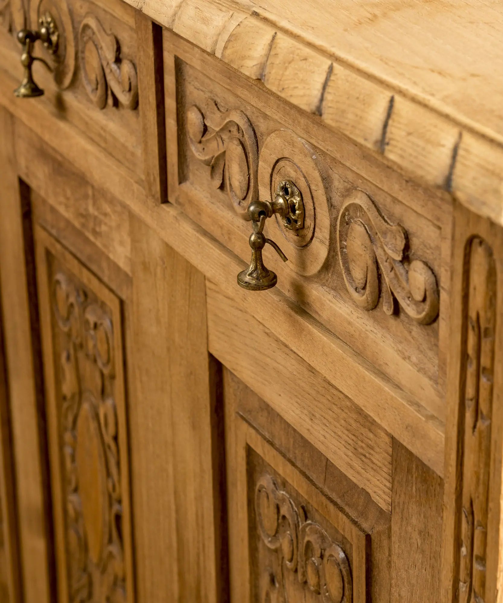 Primer plano de talla de madera en relieve y tirador de latón colgante antiguo sobre madera lavada.