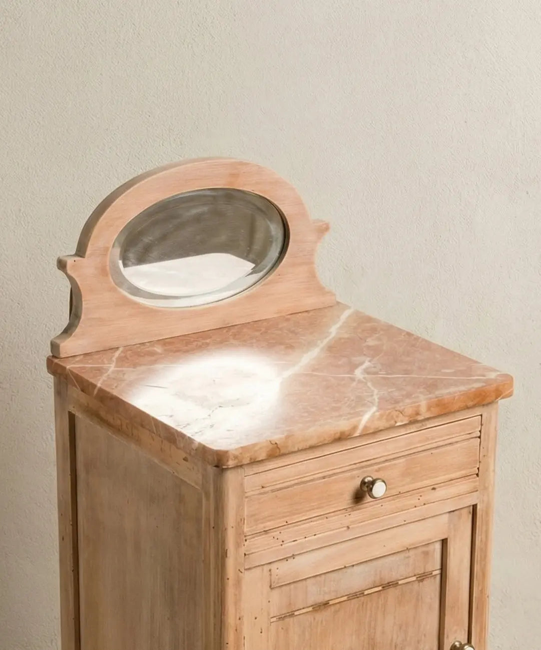 Primer plano de copete con espejo ovalado y mármol rosa veteado en mesita antigua restaurada.