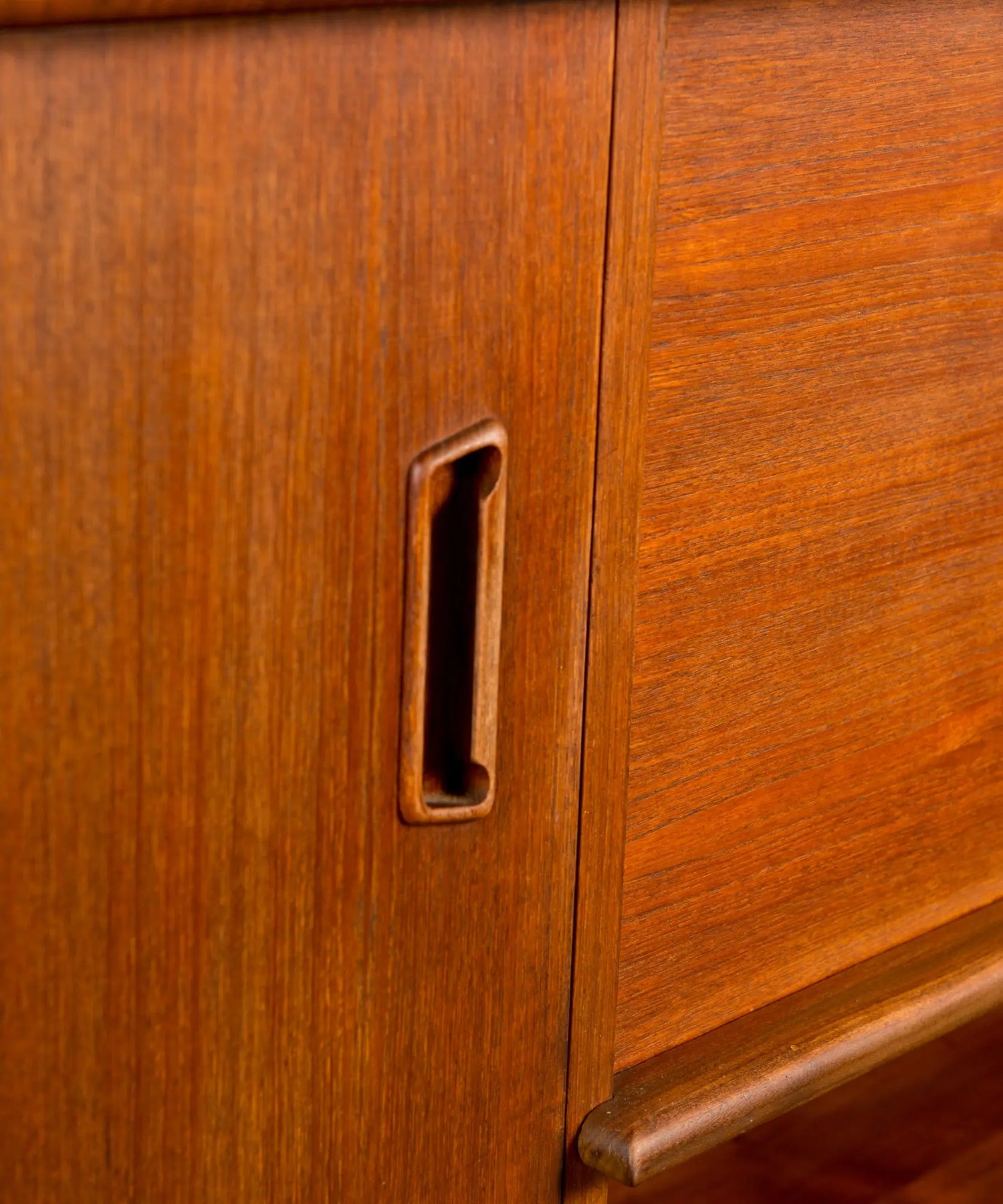 Aparador vintage de madera de teca resaltando los tiradores orgánicos y las patas cónicas.