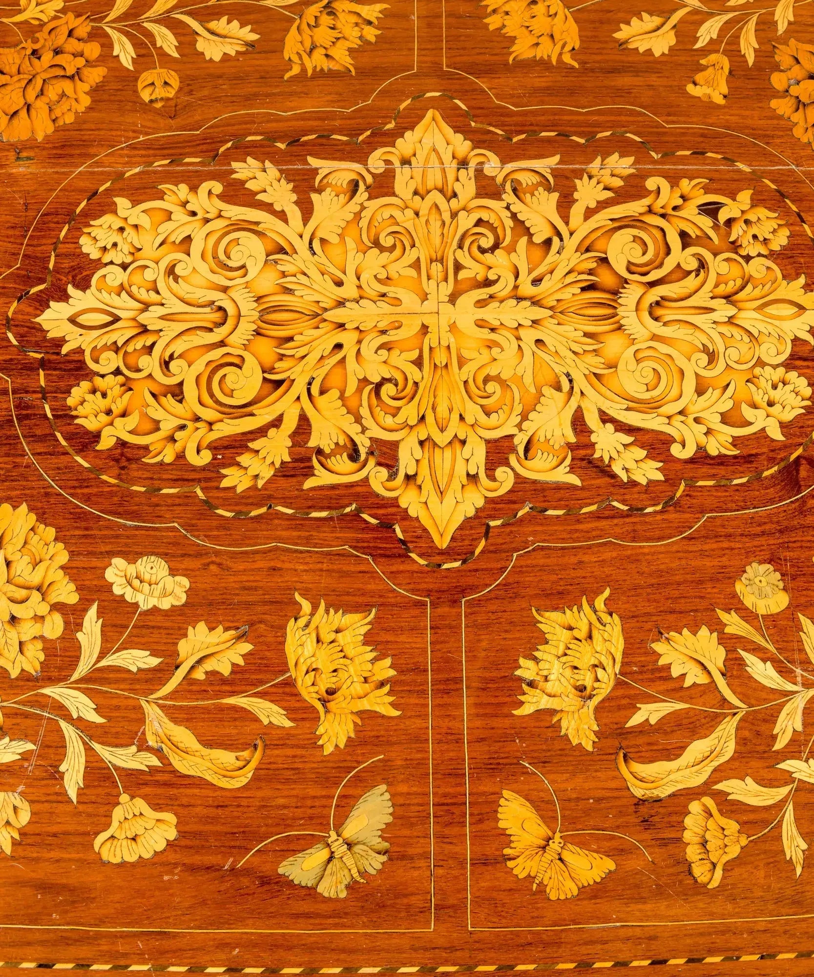 Primer plano de centro de mesa antiguo con incrustaciones artesanales de hojas de acanto y flores en madera clara.