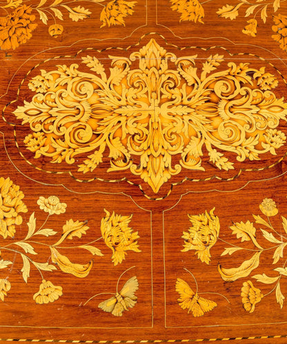 Primer plano de centro de mesa antiguo con incrustaciones artesanales de hojas de acanto y flores en madera clara.