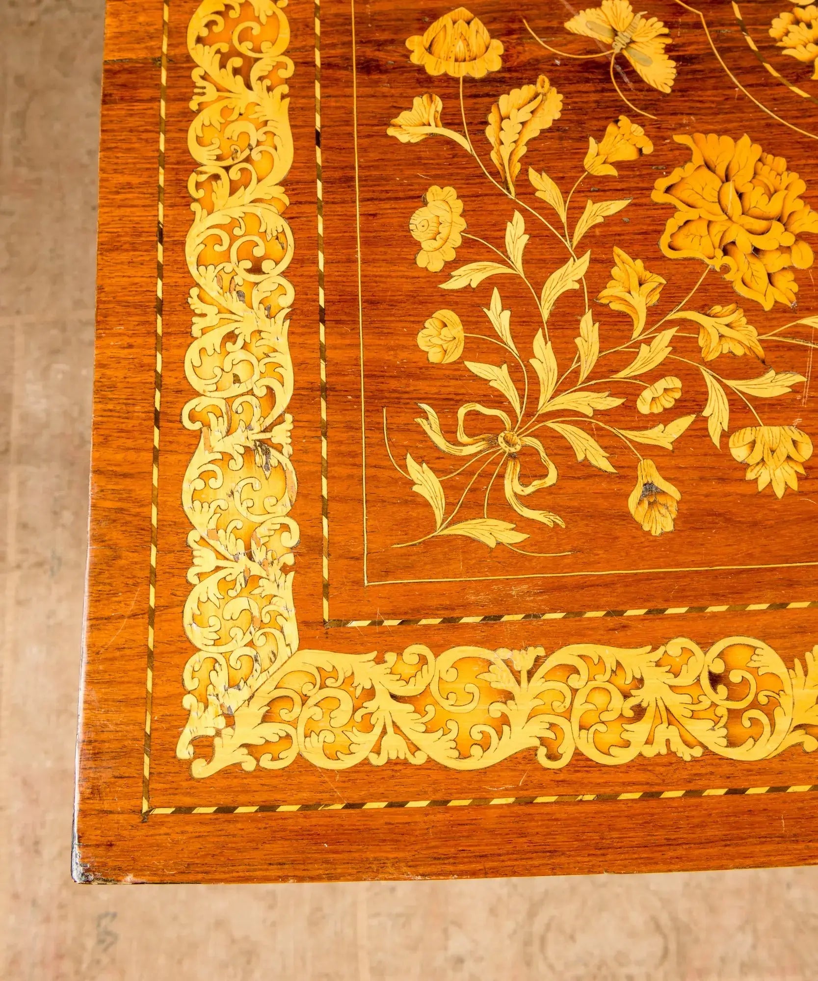 Primer plano de centro de mesa antiguo con incrustaciones artesanales de hojas de acanto y flores en madera clara.