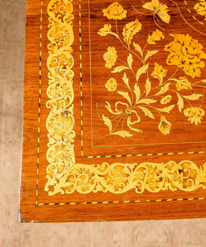 Primer plano de centro de mesa antiguo con incrustaciones artesanales de hojas de acanto y flores en madera clara.